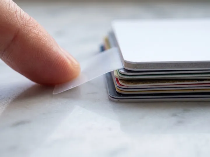 Dedos doblando una tarjeta fina junto a una pila de tarjetas de grosor estándar