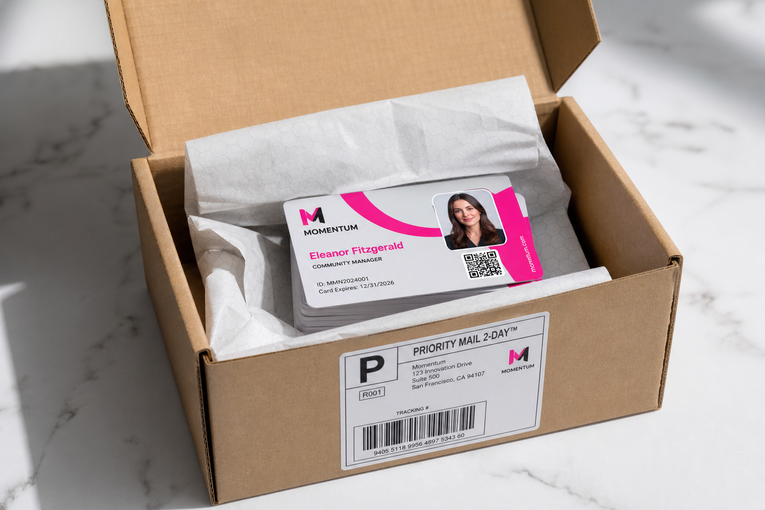 Open cardboard box revealing a stack of momentum employee id cards with a photo name eleanor fitzgerald and qr code on a pink accent design